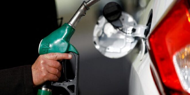 A man holds a fuel nozzle at a petrol station.